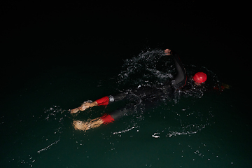 Image showing A determined professional triathlete undergoes rigorous night time training in cold waters, showcasing dedication and resilience in preparation for an upcoming triathlon swim competition