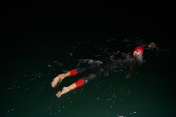 Image showing A determined professional triathlete undergoes rigorous night time training in cold waters, showcasing dedication and resilience in preparation for an upcoming triathlon swim competition