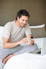 Image showing Phone, social media and laptop with a man in the bedroom of his home to relax on weekend time off. Tech, communication and person sitting on a bed while streaming a movie or series for entertainment