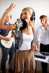 Image showing Professional, singing and happy woman with microphone, headphones and band performance with talent. Recording studio, art and girl singer live streaming for music label, sound and audio broadcast.