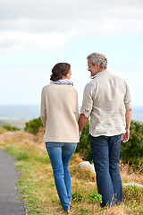 Image showing Old couple, walking and holding hands in nature on holiday, vacation or retirement with support. Back, man and woman with love, care and happiness in marriage together on a road, journey or path