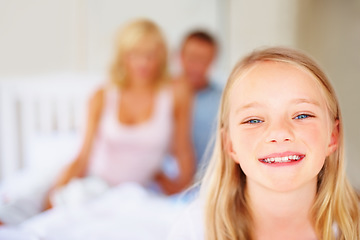 Image showing Portrait, smile and a girl in the bedroom of a home with her parents in the background to relax on a weekend. Face, kids and a happy young child on a bed in an apartment to wake up in the morning