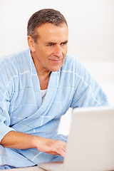 Image showing Bathrobe, relax and mature man on laptop, checking email, social media or streaming subscription on sofa. Internet website, couch and senior person on computer, morning and networking in living room.