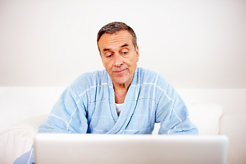 Image showing Gown, morning and mature man on laptop reading email, social media or streaming subscription on sofa. Internet search, couch and senior person in bathrobe on computer, website or networking in home.