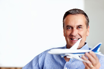 Image showing Mature man, portrait and toy plane fly for travel, vacation and holiday planning with a smile at home. Happy, airplane model and retirement of male person with confidence from trip and air traveling