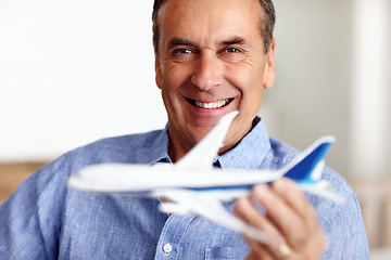 Image showing Mature man, portrait and toy plane for travel, vacation and holiday planning with a smile at home. Happy, airplane model and retirement of a male person with confidence from trip and air traveling