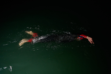 Image showing A determined professional triathlete undergoes rigorous night time training in cold waters, showcasing dedication and resilience in preparation for an upcoming triathlon swim competition