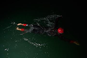 Image showing A determined professional triathlete undergoes rigorous night time training in cold waters, showcasing dedication and resilience in preparation for an upcoming triathlon swim competition