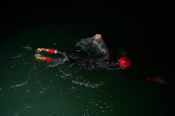 Image showing A determined professional triathlete undergoes rigorous night time training in cold waters, showcasing dedication and resilience in preparation for an upcoming triathlon swim competition