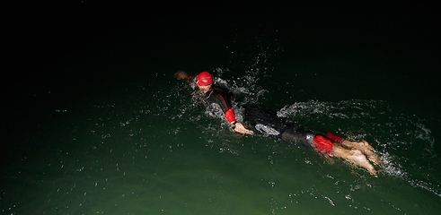 Image showing A determined professional triathlete undergoes rigorous night time training in cold waters, showcasing dedication and resilience in preparation for an upcoming triathlon swim competition