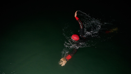 Image showing A determined professional triathlete undergoes rigorous night time training in cold waters, showcasing dedication and resilience in preparation for an upcoming triathlon swim competition