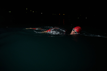 Image showing A determined professional triathlete undergoes rigorous night time training in cold waters, showcasing dedication and resilience in preparation for an upcoming triathlon swim competition