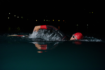 Image showing A determined professional triathlete undergoes rigorous night time training in cold waters, showcasing dedication and resilience in preparation for an upcoming triathlon swim competition