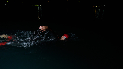 Image showing A determined professional triathlete undergoes rigorous night time training in cold waters, showcasing dedication and resilience in preparation for an upcoming triathlon swim competition