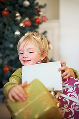 Image showing Christmas, festive and a boy opening a present under a tree in the morning for celebration or tradition. Kids, gift and excitement with an adorable young child in the living room of his home