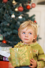 Image showing Christmas, thinking and a boy opening a present under a tree in the morning for celebration or tradition. Kids, gift and wonder with an adorable young child in the living room of his home in December