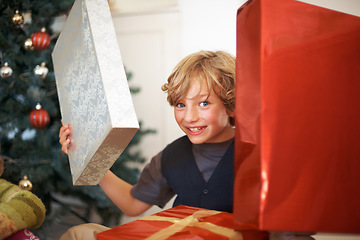 Image showing Portrait, christmas and a boy opening a present under a tree in the morning for celebration or tradition. Kids, gift and excitement with a happy, young or cute child in the living room of his home