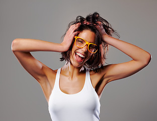 Image showing Portrait, smile and crazy with a messy hair woman in studio on a gray background for silly expression. Fashion, glasses and a happy young person feeling goofy with energy, freedom or excitement