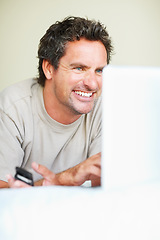 Image showing Relax, phone and laptop with a man in the bedroom of his home for entertainment on weekend time off. Smile, tech and a happy man lying in bed, streaming a movie or series while internet browsing