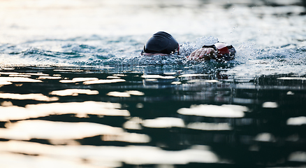 Image showing Triathlon athlete swimming on lake in sunrise wearing wetsuit