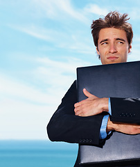 Image showing Travel, stress and business man with briefcase at beach with fear, risk or lost in nature on blue sky background. Appointment, fail and male entrepreneur hugging box at the ocean with anxiety at sea