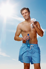 Image showing Portrait, towel and man with water for fitness, sport workout or wellness exercise outdoor in summer on blue sky. Smile, drink bottle and hydration of shirtless person, healthy body muscle and abs