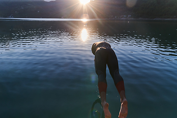 Image showing Triathlon athlete swimming on lake in sunrise wearing wetsuit