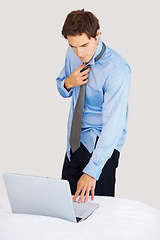 Image showing Businessman, laptop and getting ready on bed for deadline, tasks or morning schedule plan at home. Man or employee working on computer while dressing tie or suit for formal business in the bedroom