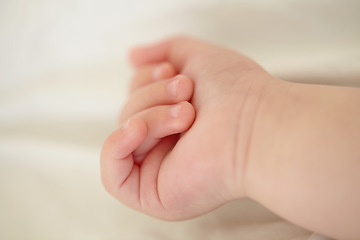 Image showing Relax, development and the hand of a baby closeup in a nursery or bedroom of a home for rest at bedtime. Kids, sleeping or wellness with the fist and fingers of a newborn infant child lying on a bed