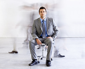 Image showing Portrait, chair and a corporate man in a busy office with motion blur people walking for company productivity. Work, business and professional with a young employee in a suit sitting in the workplace