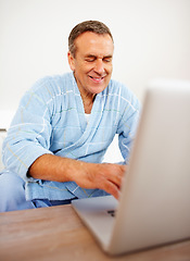 Image showing Home, bathrobe and senior man with a laptop, typing and internet with website information, smile and relax. Apartment, mature guy and person with a pc, morning and happiness with technology and email