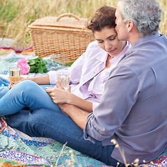 Image showing Kiss, senior couple and picnic in park, grass and basket in nature for a date or celebration with love and care. Mature, woman and man in field in summer, holiday or vacation with wine or drinks