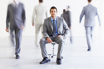 Image showing Portrait, chair and a business man in a busy office with motion blur people walking for corporate productivity. Work, company and professional with a young employee in a suit sitting in the workplace