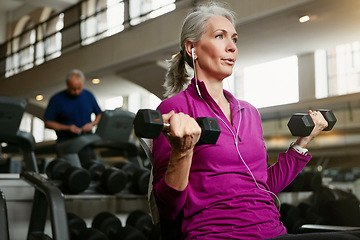 Image showing Dumbbell, fitness and senior woman at a gym for training, wellness and cardio with earphones, music or mindset. Weightlifting, bodybuilding and elderly female person at sports center for arm workout
