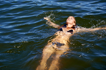 Image showing Bikini, woman and floating in water at lake to relax in summer, holiday and swimming on vacation. Calm, peace and person in swimwear, fashion or body in waves of ocean or sea with freedom in nature