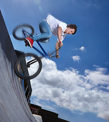 Image showing Bike, ride and teenager with speed on ramp at skatepark in summer with freedom and energy on blue sky. Fast, bicycle and performance of stunt with kid in competition, contest or event for cycling