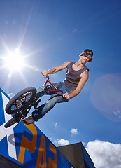 Image showing Bike, jump and man on ramp for sport performance, ride or training for summer event at park with sky. Bicycle, stunt or person on edge of board for cycling trick in competition or challenge with risk