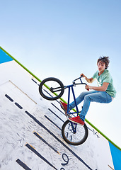 Image showing Bike, trick and teenager in the air at skatepark with energy in performance for competition or event in summer. Bicycle, jump or stunt on wall with score, board and fearless freedom of cyclist in sky