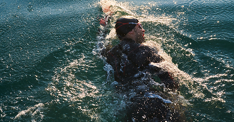 Image showing Triathlon athlete swimming on lake in sunrise wearing wetsuit