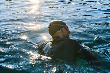 Image showing Triathlon athlete swimming on lake in sunrise wearing wetsuit