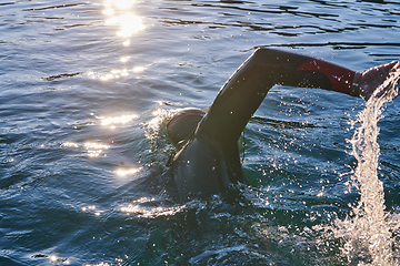 Image showing Triathlon athlete swimming on lake in sunrise wearing wetsuit