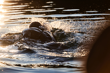 Image showing Triathlon athlete swimming on lake in sunrise wearing wetsuit