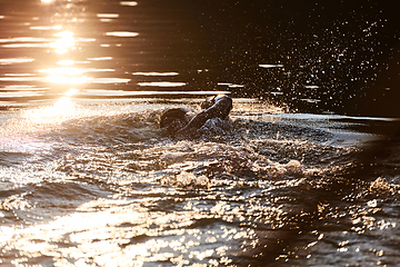 Image showing Triathlon athlete swimming on lake in sunrise wearing wetsuit