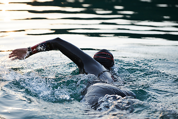 Image showing Triathlon athlete swimming on lake in sunrise wearing wetsuit