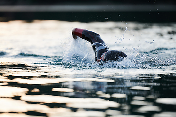 Image showing Triathlon athlete swimming on lake in sunrise wearing wetsuit