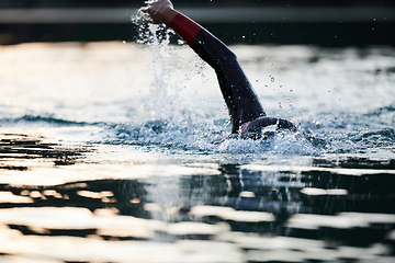 Image showing Triathlon athlete swimming on lake in sunrise wearing wetsuit