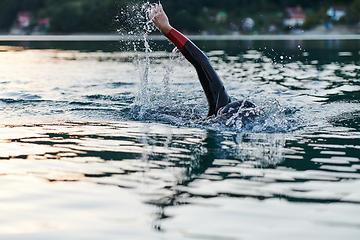 Image showing Triathlon athlete swimming on lake in sunrise wearing wetsuit