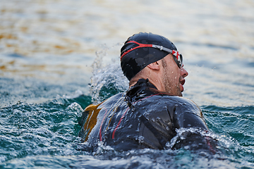 Image showing Triathlon athlete swimming on lake in sunrise wearing wetsuit