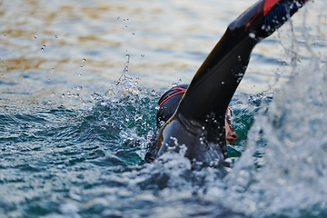 Image showing Triathlon athlete swimming on lake in sunrise wearing wetsuit