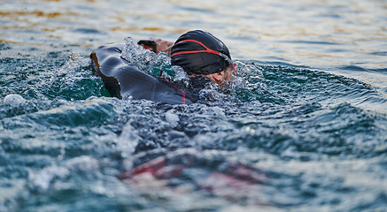 Image showing Triathlon athlete swimming on lake in sunrise wearing wetsuit